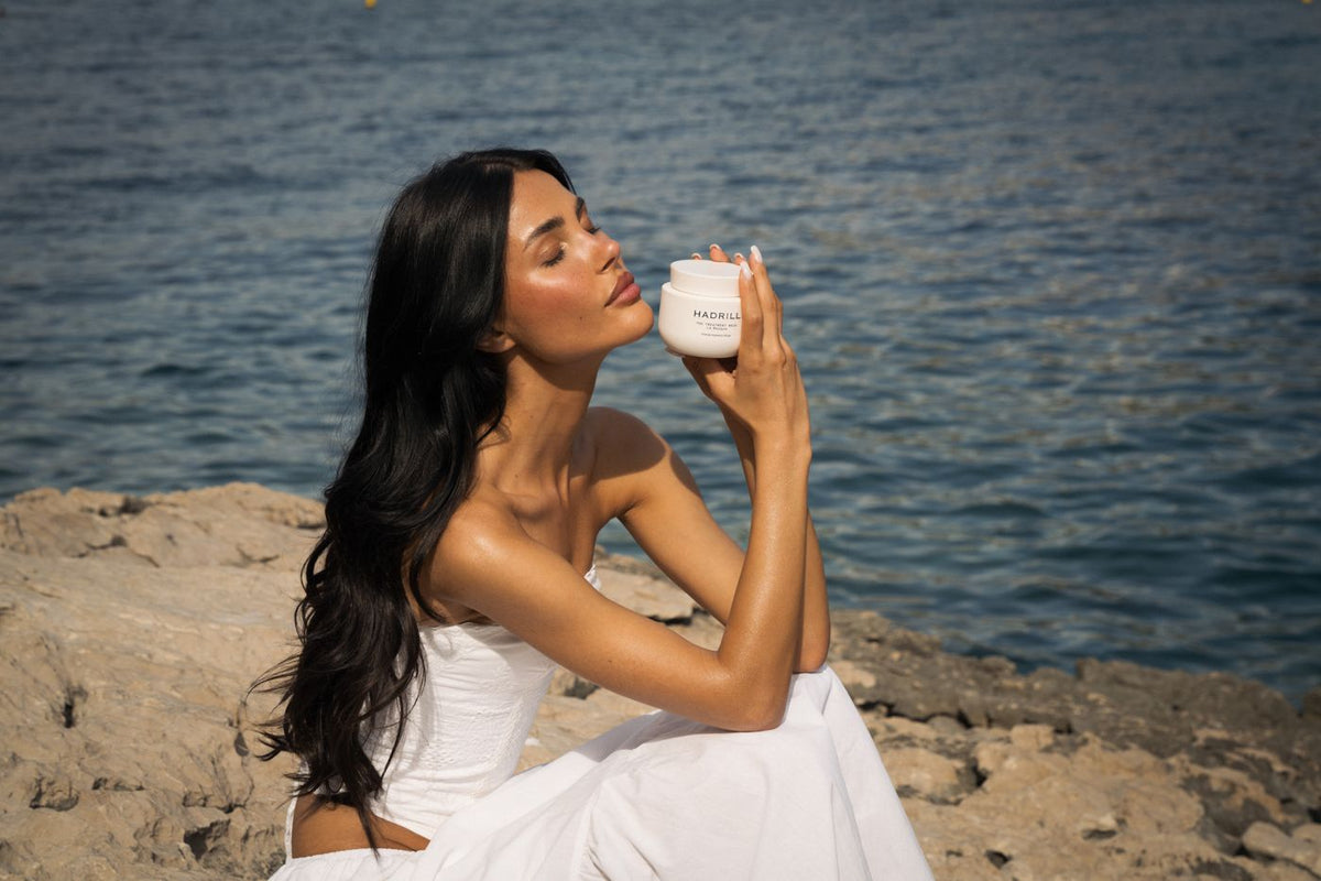 Woman with long dark hair holding Hadrill The Treatment Mask beside the sea